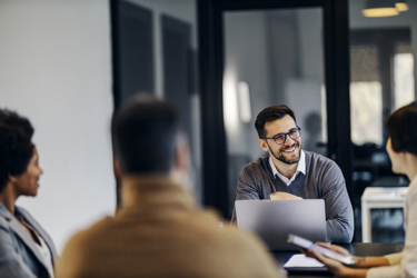 A group of people at work sit around a meeting table talking